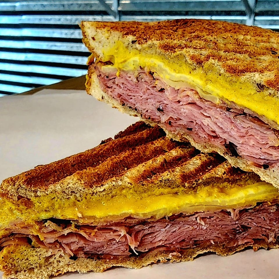 A grilled sandwich from Yellow Mustard, cut in half, revealing layers of meat, cheese, and yellow mustard.