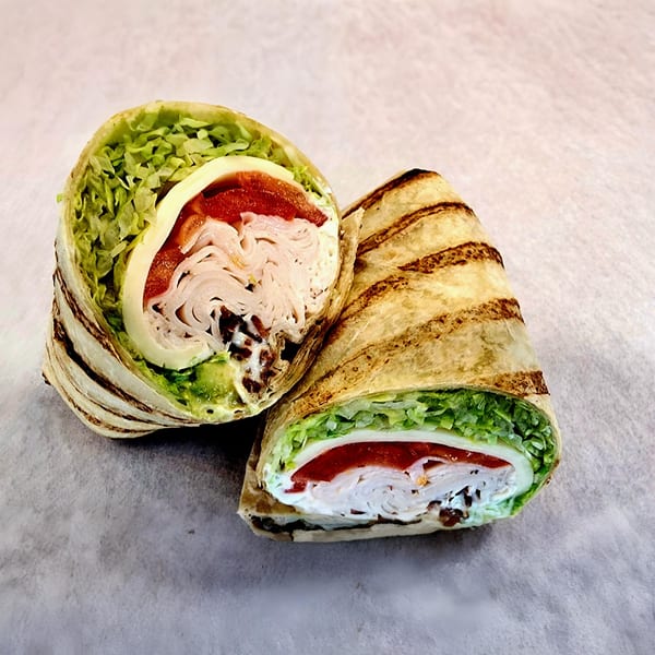 Two halves of a grilled turkey wrap, filled with lettuce, cheese, red peppers, and sauce.