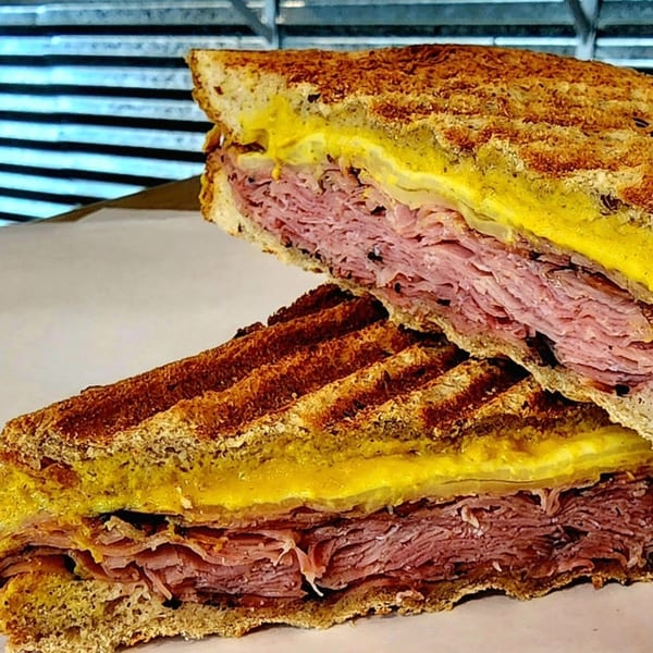 A grilled sandwich from Yellow Mustard, cut in half, revealing layers of meat, cheese, and mustard.