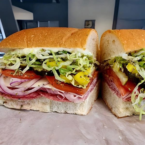 A large Yellow Mustard sandwich, cut in half, filled with meats, cheese, lettuce, tomatoes, and onions.