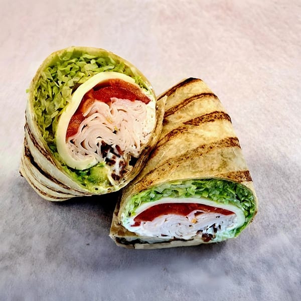 Two halves of a grilled turkey wrap with lettuce, cheese, and red peppers.
