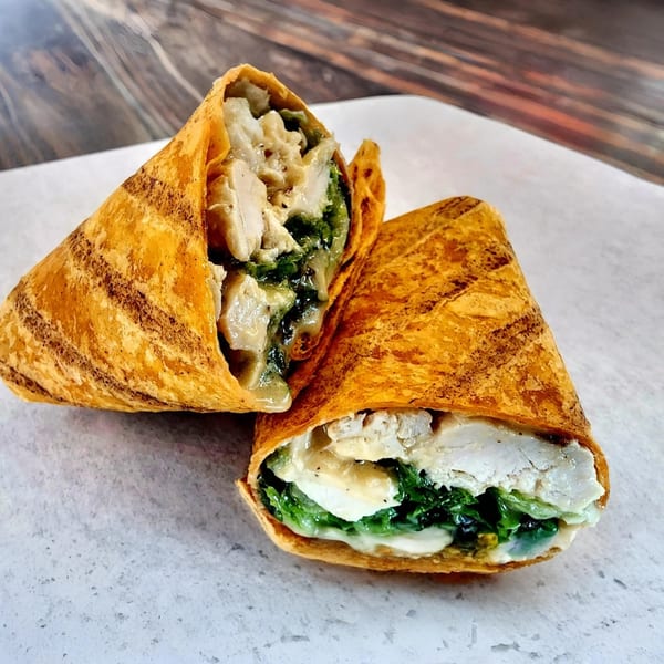 Two halves of a Yellow Mustard chicken and spinach wrap, filled with creamy sauce, on a white surface.